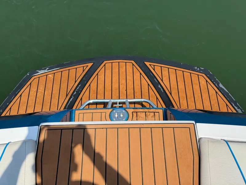 Slide: The Image of 2014 Nautique Sport 200 boat deck with teak flooring, overlooking green water. - 8