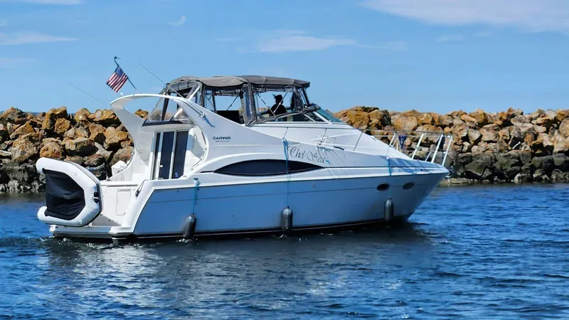 The Image of 1997 Carver 350 Mariner yacht cruising near rocky shoreline under clear blue sky. - 1