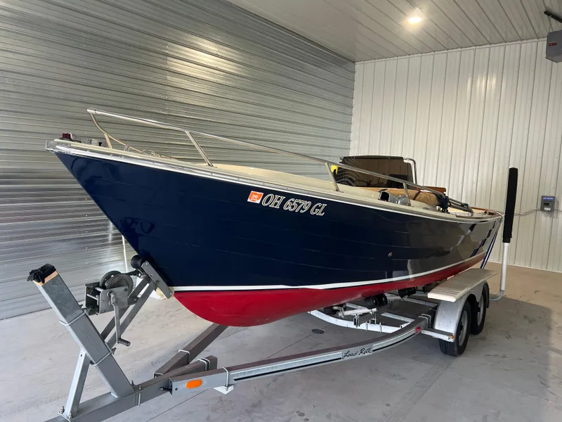 The Image of 1974 Chris-Craft Dory boat on trailer in garage, blue and red hull. - 0