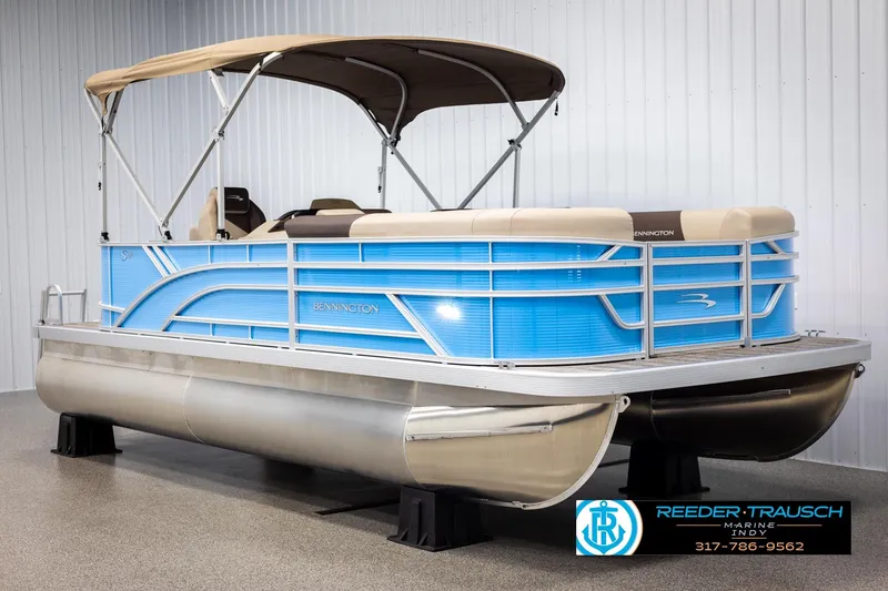 Slide: The Image of 2025 Bennington 21 SL pontoon boat with blue exterior and beige canopy in showroom. - 2