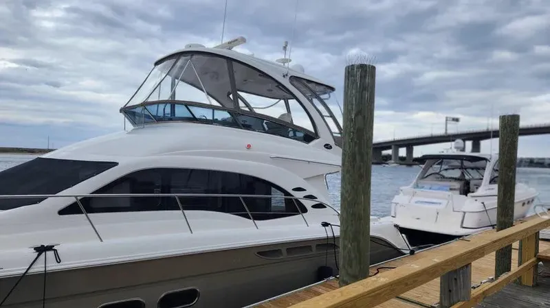 Slide: The Image of 2006 Sea Ray 52 Sedan Bridge yacht docked by a wooden pier under cloudy skies. - 10