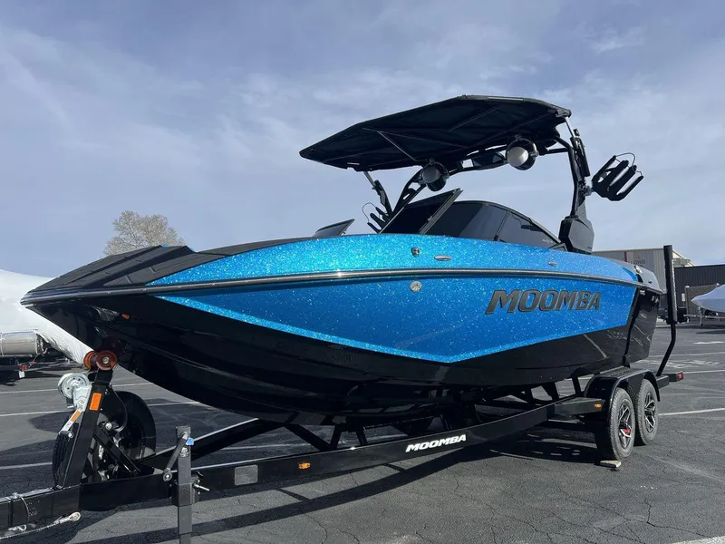 Slide: The Image of 2025 Moomba Mojo boat with blue glitter finish on a trailer, parked outdoors. - 1