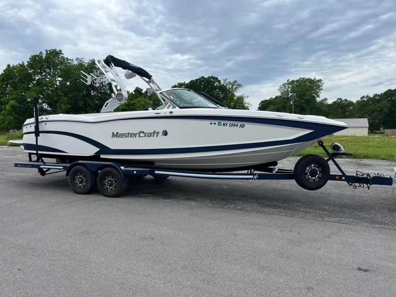 The Image of 2019 MasterCraft X26 boat on trailer, parked outdoors with cloudy sky background. - 0