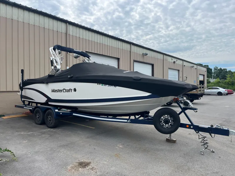 Slide: The Image of 2019 MasterCraft X26 boat on trailer, parked outside industrial building. - 2