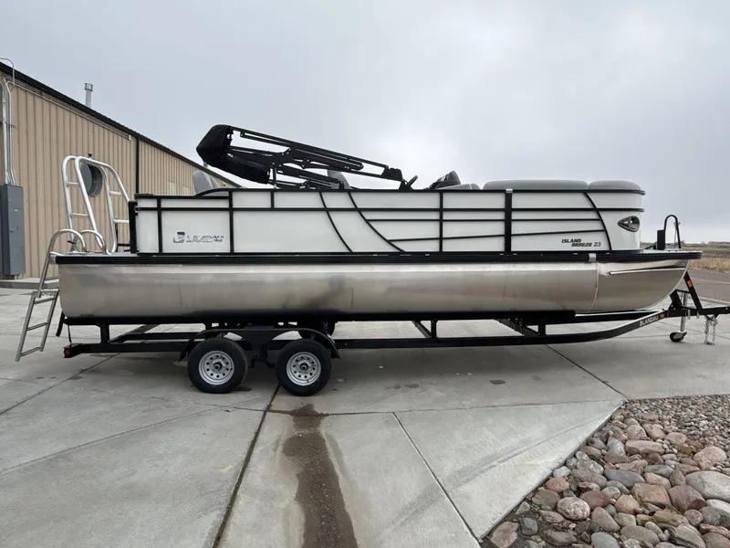 Slide: The Image of 2025 Landau ISLAND BREEZE 23 pontoon boat on trailer, parked outdoors. - 6