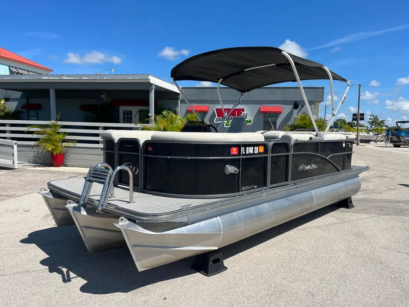 Slide: The Image of 2020 Manitou 20 Aurora LE Standard pontoon boat with black canopy, parked outdoors. - 1