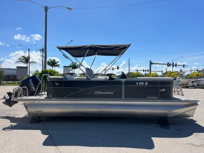 Slide: The Image of 2020 Manitou 20 Aurora LE Standard pontoon boat with Suzuki outboard motor, parked outdoors. - 4