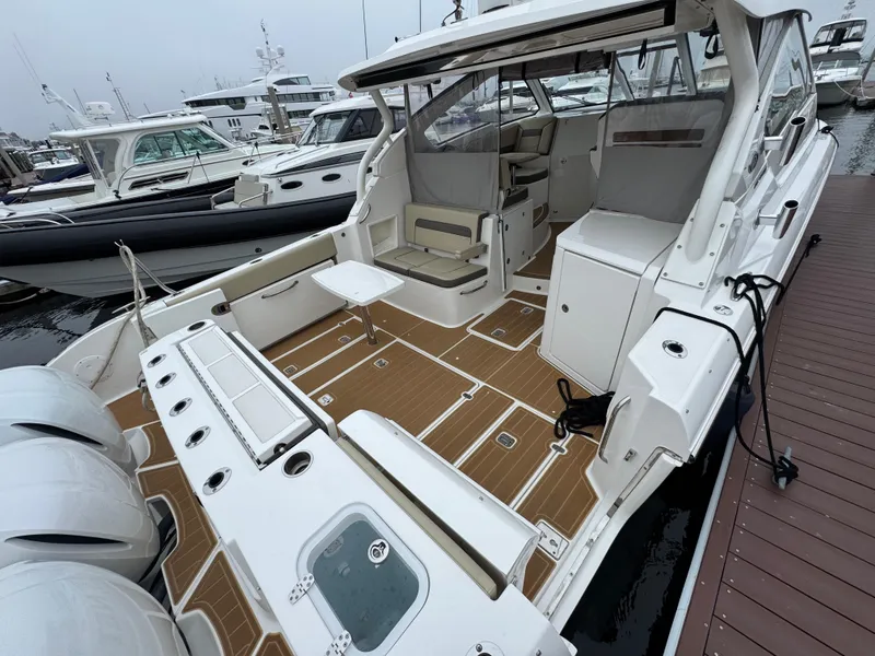 Slide: The Image of 2019 Pursuit DC 365 Dual Console boat docked, featuring spacious deck and seating area. - 6
