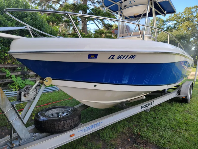 Slide: The Image of 2012 Carolina Skiff 24 boat on trailer, blue and white design, parked on grass. - 2