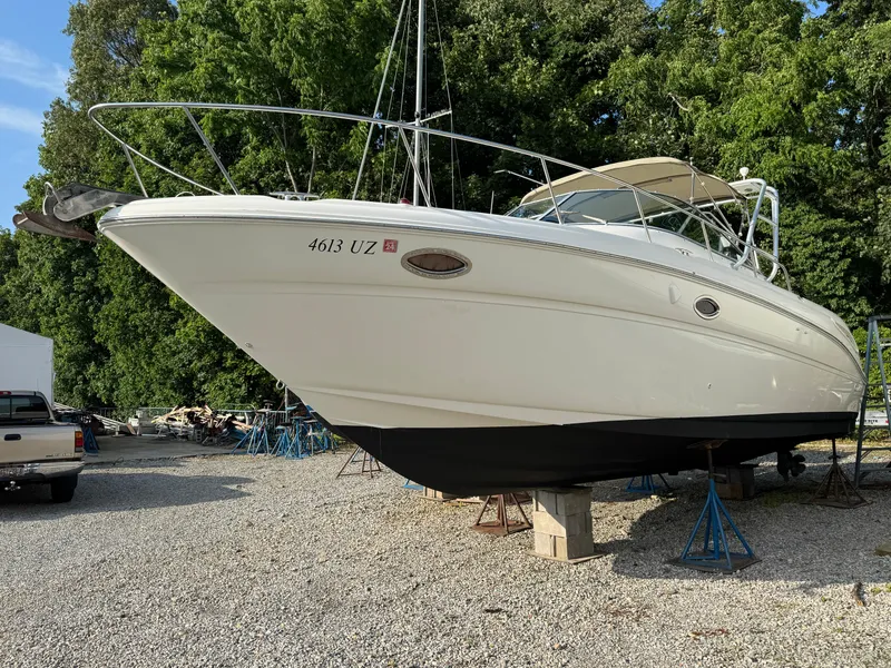 The Image of 2003 Sea Ray 290 Amberjack boat on stands, surrounded by trees and gravel. - 0