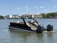 Slide: The Image of 2022 Bennington 30 RSRAX2 pontoon boat on a calm lake with buildings in the background. - 6