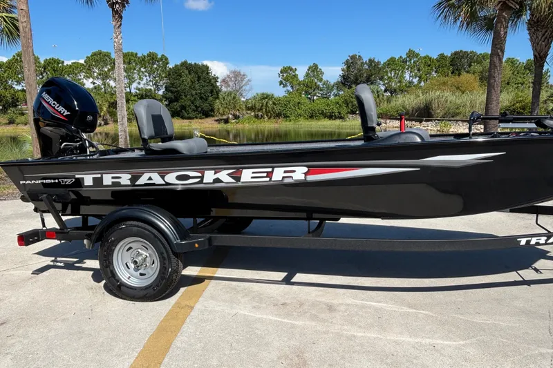 The Image of 2025 Tracker Panfish 17 boat on trailer, parked near a scenic lake with palm trees. - 0