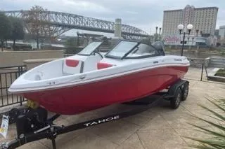 The Image of 2025 Tahoe 200 S boat in red on a trailer, urban background with bridge. - 0