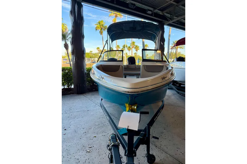 The Image of 2025 Tahoe 200 S boat on trailer, parked indoors with palm trees visible outside. - 0