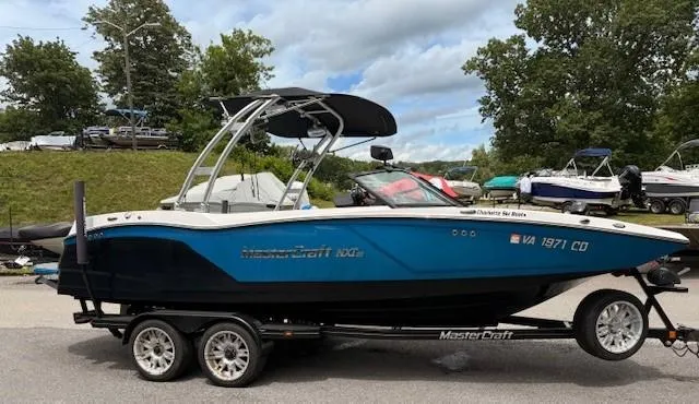 The Image of 2017 MasterCraft NXT22 boat on trailer, blue and white design, parked outdoors. - 0