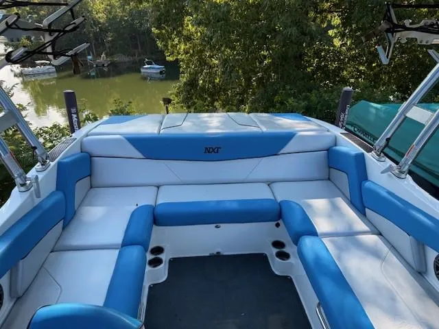 Slide: The Image of 2017 MasterCraft NXT22 boat interior with blue and white seating, docked by a scenic lake. - 10
