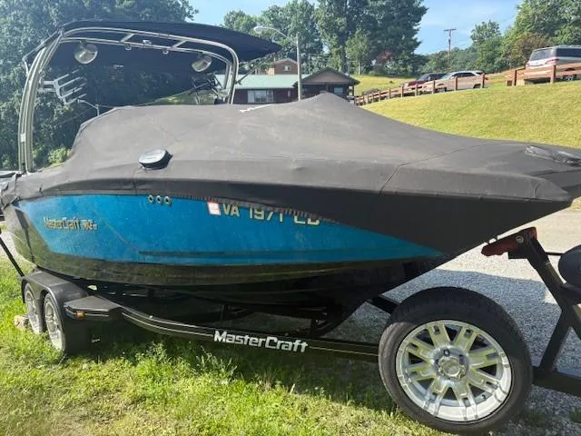 Slide: The Image of 2017 MasterCraft NXT22 boat on trailer, covered, parked on grass with trees and houses in background. - 2