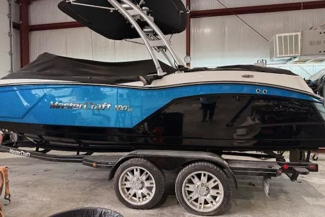 Slide: The Image of 2017 MasterCraft NXT22 boat in a garage, featuring a blue and black design on a trailer. - 38