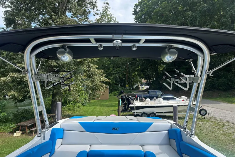 Slide: The Image of 2017 MasterCraft NXT22 boat with blue seating and wakeboard racks, parked near trees. - 41