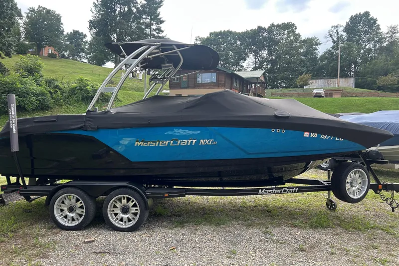 Slide: The Image of 2017 MasterCraft NXT22 boat on trailer, covered, parked outdoors with trees and buildings in background. - 44