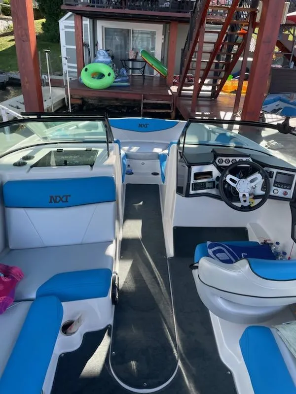 Slide: The Image of 2017 MasterCraft NXT22 boat interior with blue and white seating, docked near a lakeside house. - 9