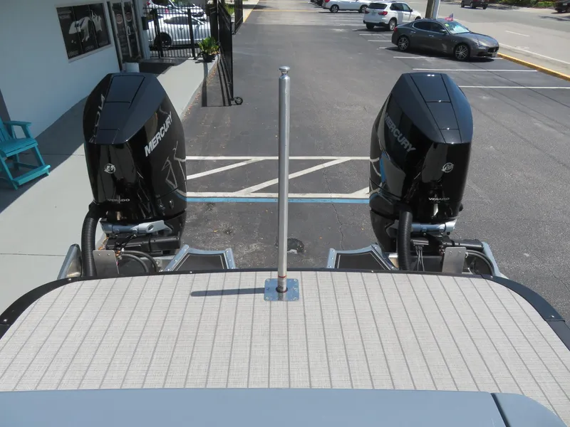Slide: The Image of 2026 Avalon Excalibur Elite Windshield boat with dual Mercury outboard engines in parking lot. - 14