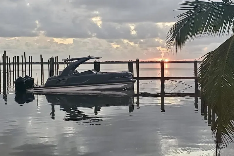 Slide: The Image of 2026 Avalon Excalibur 27' boat docked at sunset, with palm tree and calm water. - 8
