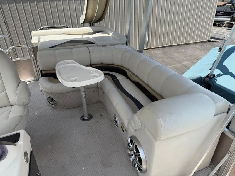 Slide: The Image of 2011 Tahoe Pontoon Double Decker with white seating and table, docked near a metal building. - 15