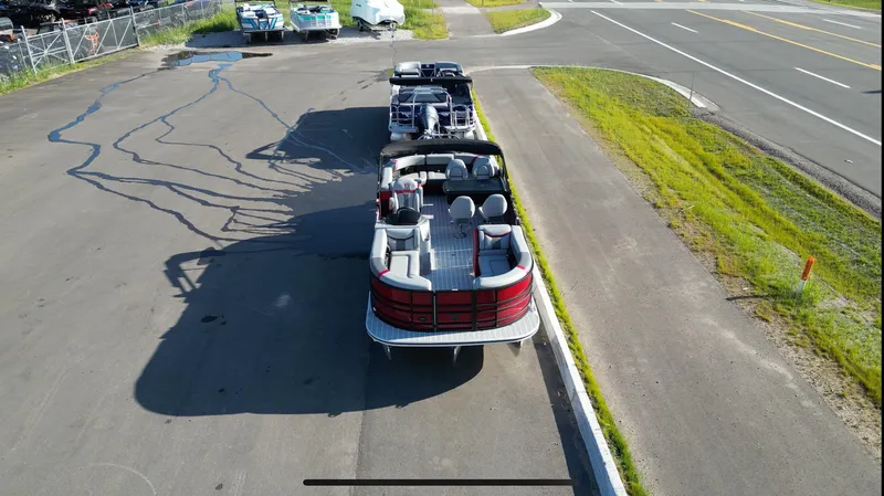 Slide: The Image of 2025 Trifecta 24ECS275 pontoon boat parked on a paved lot, aerial view. - 2