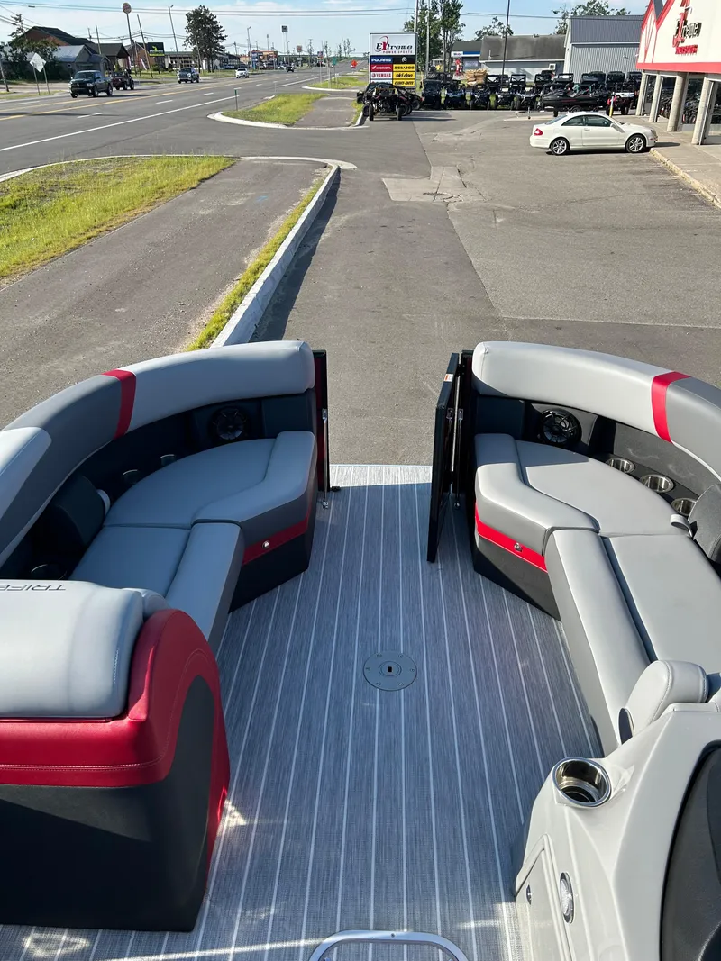 Slide: The Image of 2025 Trifecta 24ECS275 pontoon boat interior with gray and red seating, parked near a dealership. - 3