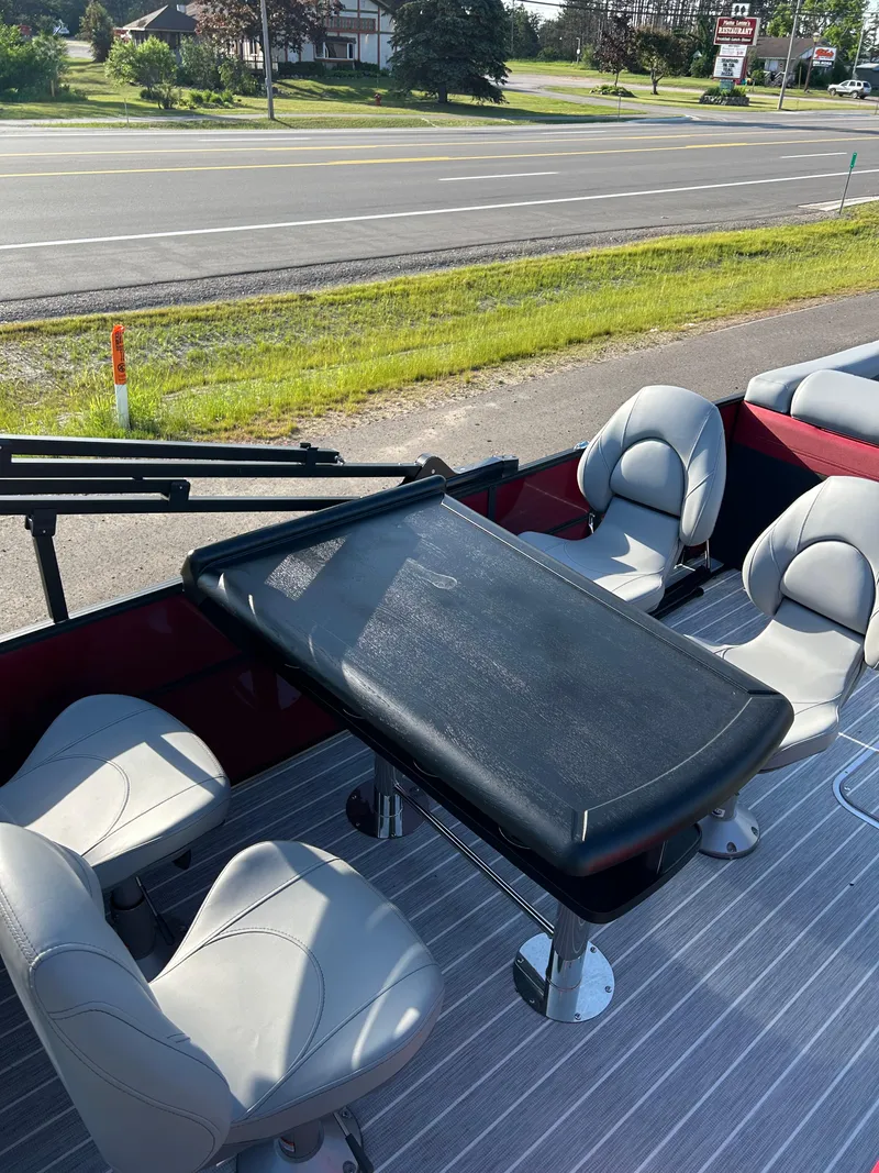 Slide: The Image of 2025 Trifecta 24ECS275 pontoon boat interior with seating and table, parked roadside. - 5