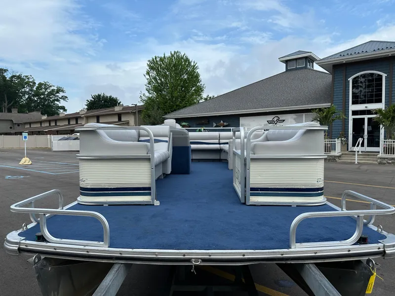 Slide: The Image of 1997 Suncruiser 22 pontoon boat with blue carpet and white seating, parked near a building. - 3