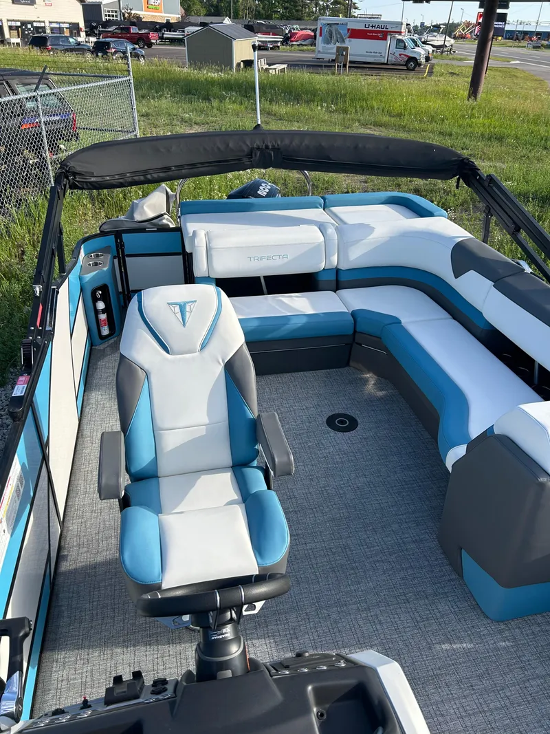 Slide: The Image of 2024 Trifecta 25C SS pontoon boat interior with blue and white seating, steering chair, and canopy. - 3