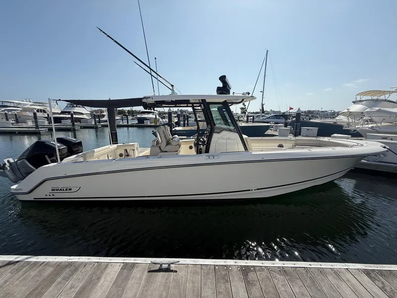 The Image of 2021 Boston Whaler 330 Outrage docked at marina under clear blue sky. - 0