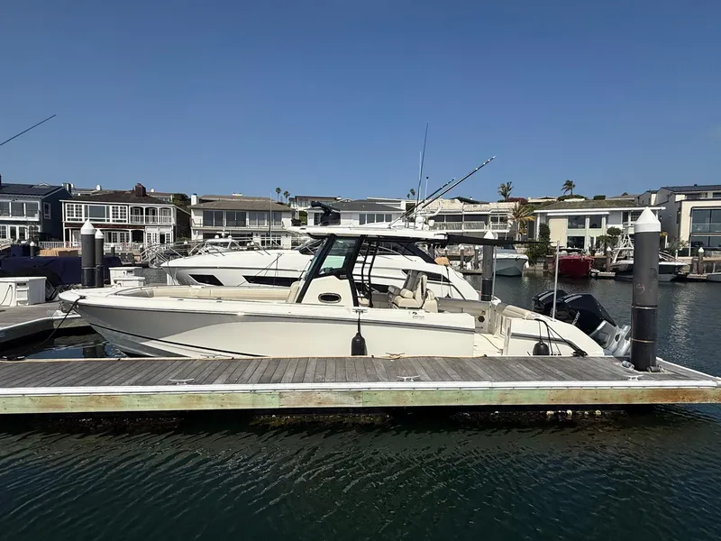 Slide: The Image of 2021 Boston Whaler 330 Outrage docked in a marina with waterfront homes in the background. - 7
