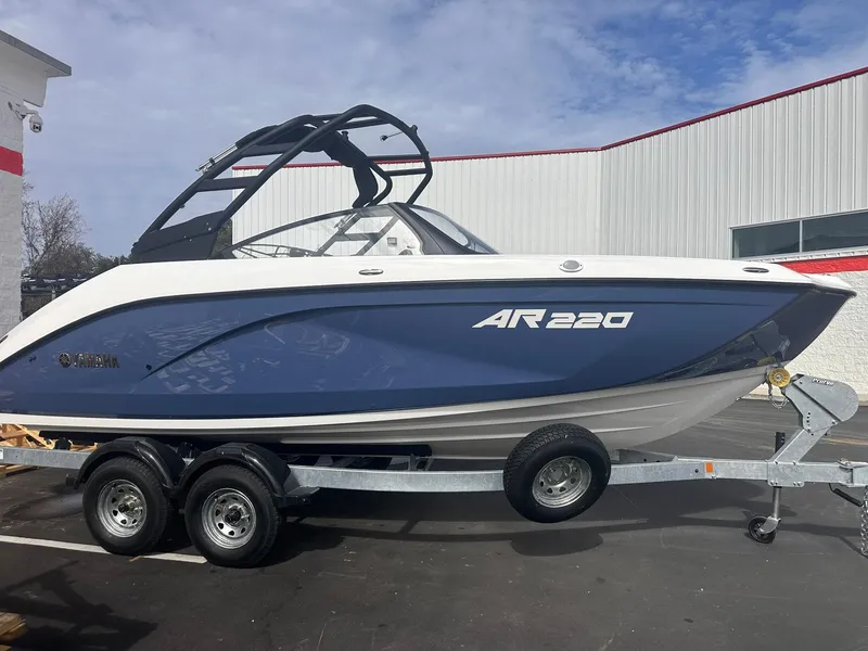 The Image of 2025 Yamaha Boats AR220 on trailer, blue and white design, parked outdoors. - 0