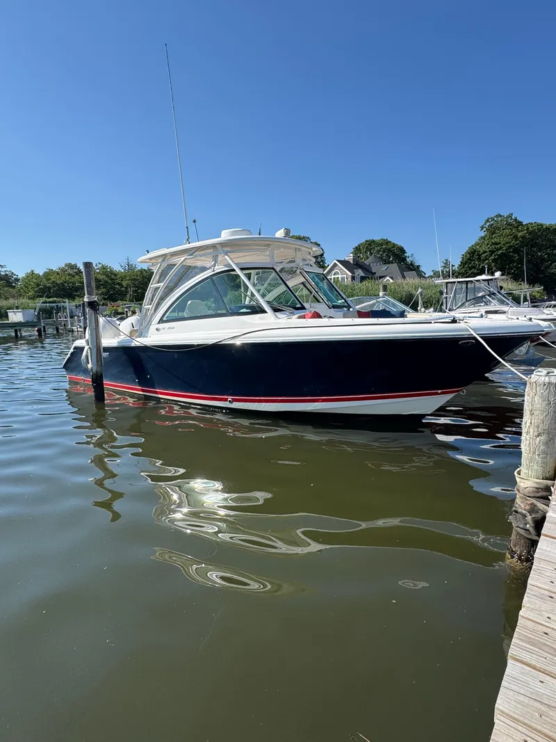 The Image of 2016 Pursuit DC 265 Dual Console boat docked in a marina under clear blue sky. - 0