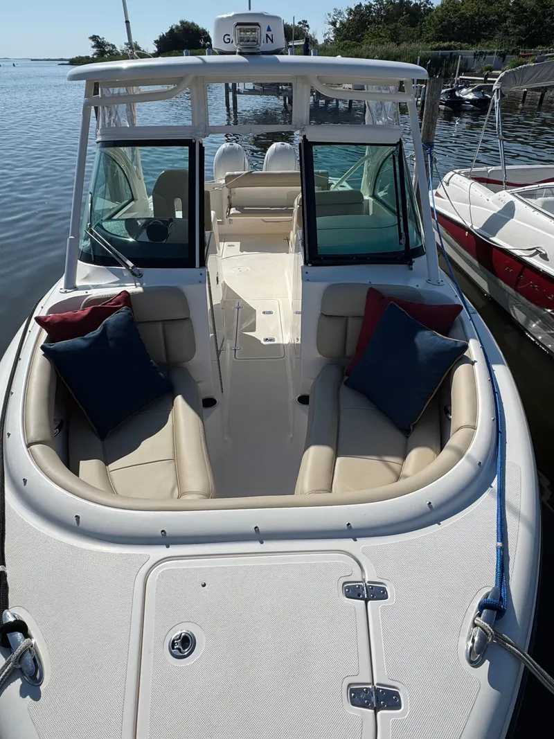 Slide: The Image of 2016 Pursuit DC 265 Dual Console boat with cushioned seating and pillows, docked by the water. - 11