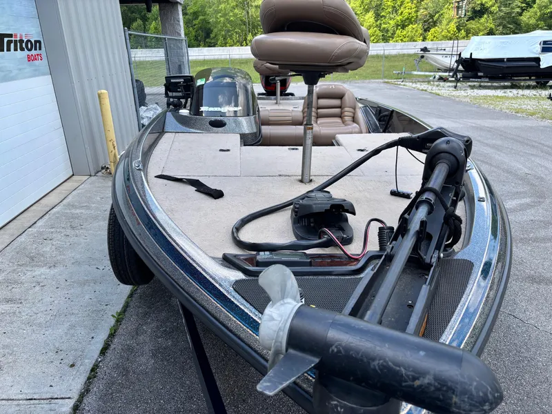 Slide: The Image of 2000 Ranger 518VX Comanche boat with trolling motor and seating, parked near Triton Boats facility. - 4