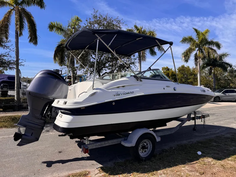 Slide: The Image of 2017 Hurricane 2000SD boat on trailer, parked near palm trees under a clear blue sky. - 6