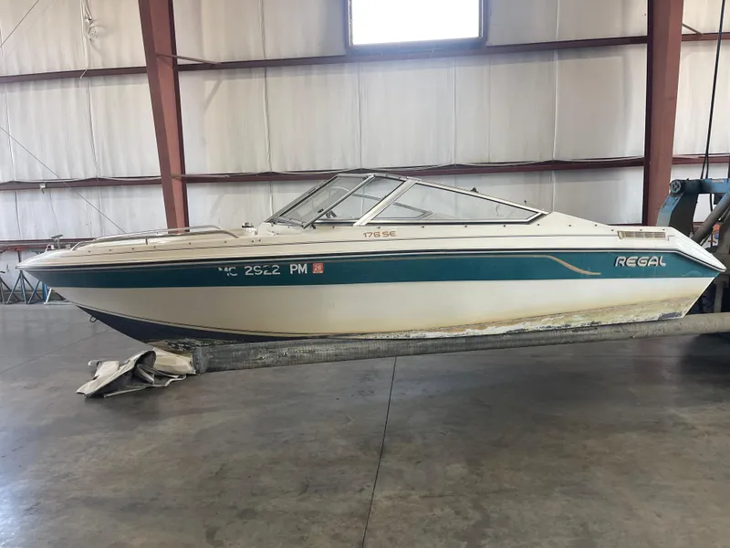 Slide: The Image of 1993 Regal 176 SE boat in warehouse, side view, white and teal design. - 2