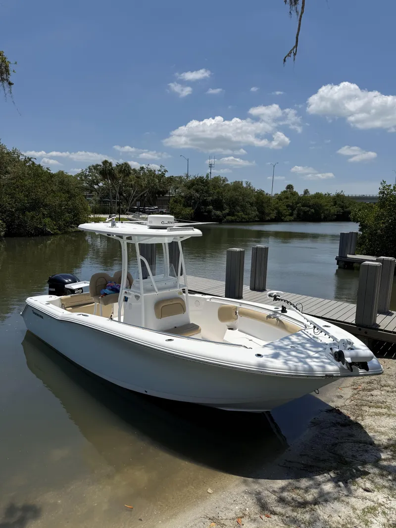 The Image of 2016 Tidewater 230 CC Adventure boat docked by a serene river under a clear blue sky. - 0