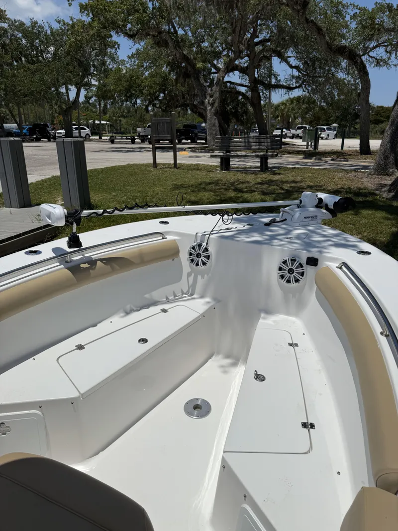 Slide: The Image of 2016 Tidewater 230 CC Adventure boat interior with seating and speakers, parked near trees. - 9