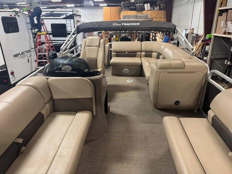 Slide: The Image of 2021 Sun Tracker Party Barge 20 DLX interior with beige seating and helm in a garage. - 5