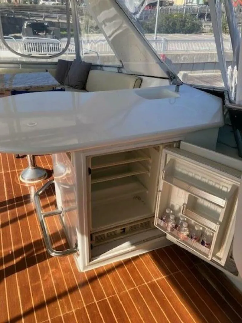 Slide: The Image of 1996 Hatteras 70 Sport Deck Motor Yacht interior with bar, open fridge, and wooden flooring. - 7