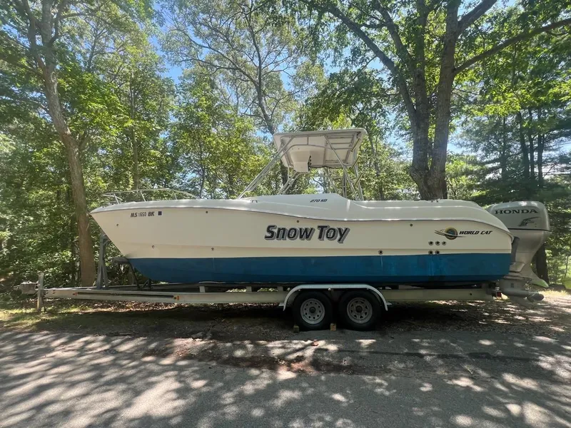 The Image of 2007 World Cat 266 SD boat named "Snow Toy" on trailer, surrounded by trees. - 0