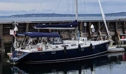 Slide: The Image of 1990 Jeanneau Sun Magic 44 sailboat docked at a marina, with calm water and distant hills. - 0