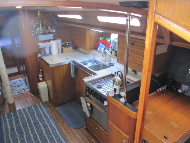 Slide: The Image of Interior of 1990 Jeanneau Sun Magic 44 yacht, featuring a compact kitchen and wooden cabinetry. - 15