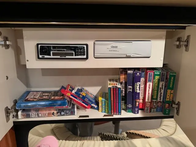 Slide: The Image of Cabinet with VHS tapes and player inside a 1999 Sea Ray 38' Sundancer boat. - 46