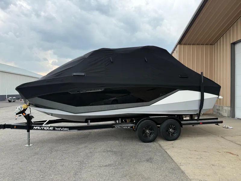 Slide: The Image of 2025 Nautique Super Air Nautique G23 boat covered on trailer, parked outside a building. - 21